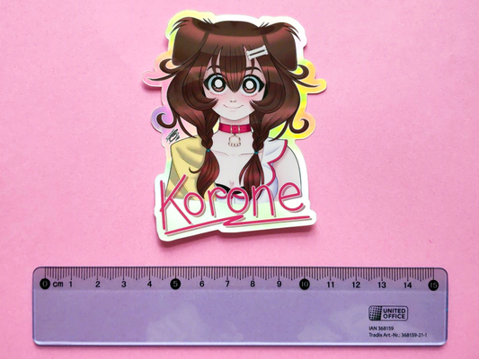 Photo of a holographic sticker of hololive vtuber Inugami Korone illustrated from the bust up. There's a blue ruler underneath it to show a size comparison.