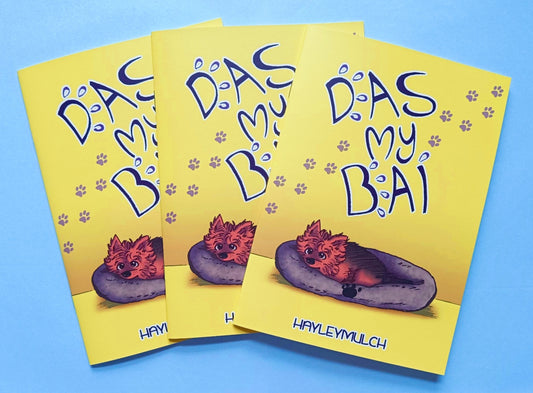 Three copies of the comic Das My Bai. It's a mostly yellow book cover with a dog in a bed and the title of the book written in big text.