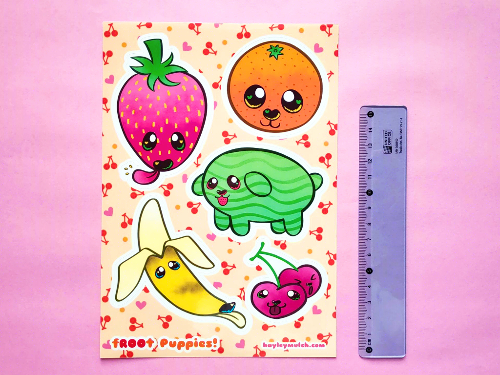 Photo of an A5 sticker sheet displayed across a pink background. The stickers are of a strawberry, orange, watermelon, banana and cherries and they have puppy faces. A blue transparent ruler is next to it for size comparison.