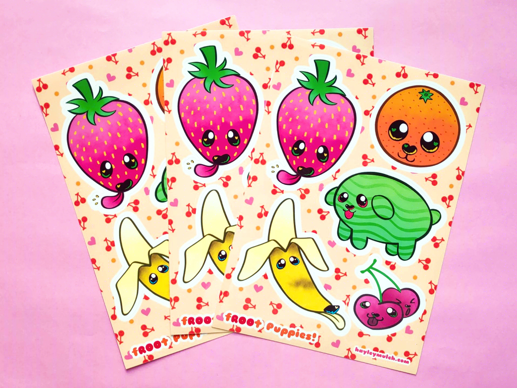 Photo of three A5 sticker sheets fanned out across a pink background. The stickers are of a strawberry, orange, watermelon, banana and cherries and they have puppy faces.