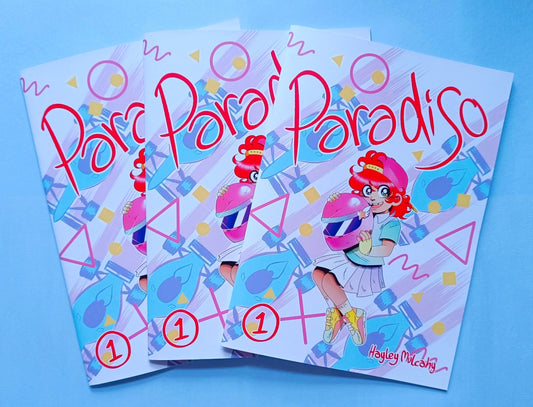 Three printed copies of my comic, Paradiso, with the titular character Tiffany Paradiso, a 7 year old white girl with red hair, holding a pink racing helmet on the cover.