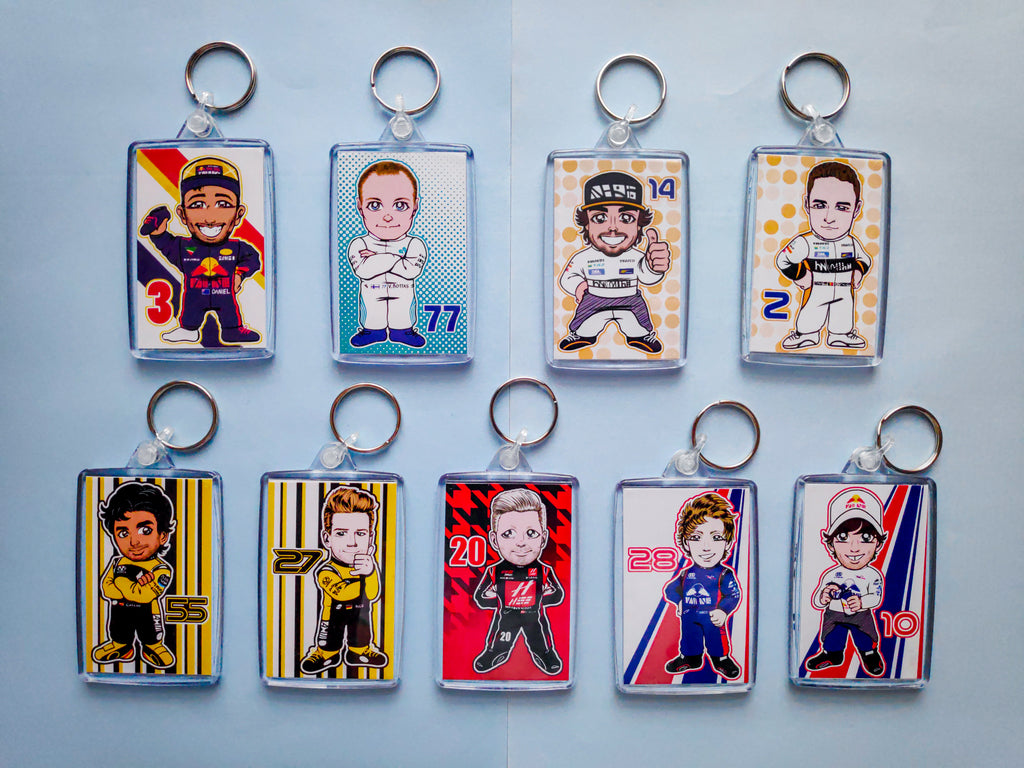 Image of 9 rectangular keychains depicting the various F1 drivers from the 2018 season in chibi style: Daniel Ricciardo, Valtteri Bottas, Fernando Alonso, Stoffel Vandoorne, Carlos Sainz, Nico Hulkenberg, Kevin Magnussen, Brendan Hartley and Pierre Gasly. They are placed against a light blue background.