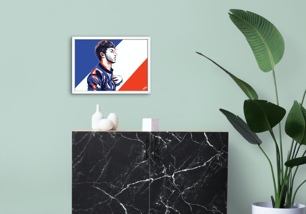 The aforementioned Pierre Gasly illustration shown in a mock-up display frame for real life reference. It's in a white frame, hung on a sage green wal, above a black marble mantle piece with white ornaments placed upon it. A green, tall indoor plant is placed to the right.