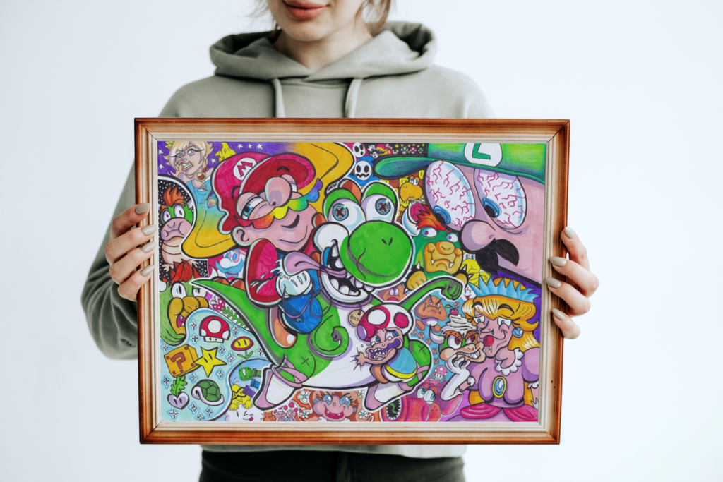The aforementioned Super Mario illustration shown in a mock-up display frame for real life reference. It's shown in a landscape A3 wooden frame, which someone is holding up from behind. They are wearing a light green hoodie with black pants. They are smiling but the rest of the head is out of shot.
